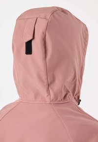 Artimųjų planas dulkių rožinės spalvos striukės gobtuvu su juoda lipnia juostele ir matomomis siūlėmis ant vientisos spalvos fono.