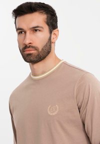 Camicia a maniche lunghe marrone con colletto in tonalità chiara a contrasto e logo ricamato sul petto; tessuto morbido e strutturato.