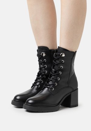 Black leather ankle boots with a block heel, featuring a lace-up front, silver eyelets, and a textured sole for grip.