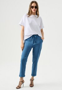 T-shirt blanc à coupe décontractée avec des manches retroussées, associé à un jogger en satin bleu clair avec une taille élastique et des poignets, accentué par des talons à lanières.