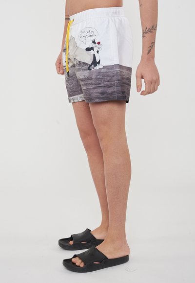 Costumi da bagno con un design bianco e grigio, cordoncino giallo e un personaggio dei cartoni animati su un lato, abbinati a infradito nere.