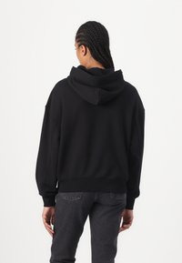 Zwarte hoodie met een relaxte pasvorm, geribde mouwen en tailleband. Glad textuur en een eenvoudig ontwerp, gedragen met donkergrijze jeans.