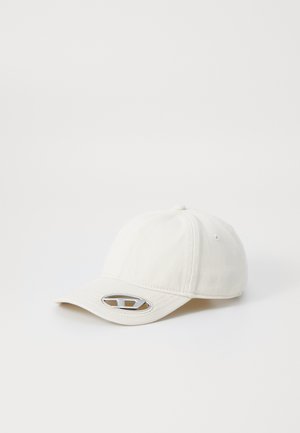 Casquette de baseball couleur crème avec une visière courbée, en tissu texturé, et un logo métallique argenté à l'avant. Quatre trous de ventilation présents.
