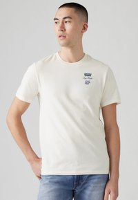 Short-sleeve cream t-shirt made of cotton, featuring a navy Levi's logo and text, round neckline, and a fitted design.