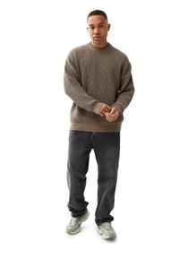 Strikket sweater i beige med et struktureret mønster, parret med mørkegrå baggy jeans og grønligt-grå sneakers. Afslappet pasform med sænkede skuldre.