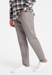 Pantalon gris ajusté en tissu doux, présentant une texture lisse, des poches latérales et associé à des baskets blanches.