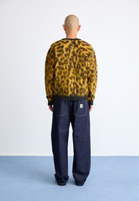 Søt gul og svart leopardmønstrete genser sammen med mørkeblå vide jeans med baklommer og logo-patch.