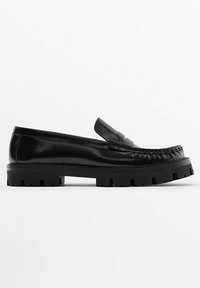 Mocassin noir en cuir avec semelle en caoutchouc épaisse et couture de style mocassin sur fond blanc, vue latérale.