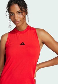 Red sleeveless athletic top made of smooth fabric; features a high neck and a black Adidas logo on the front center.