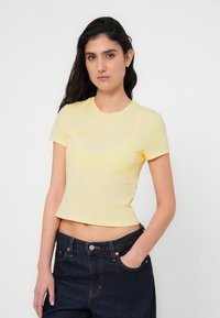 Keltainen, lyhythihainen, istuva t-paita, joka on valmistettu pehmeästä kankaasta ja jossa on pyöreä pääntie, yhdistetty tummiin, korkeavyötäröisiin farkkuihin.