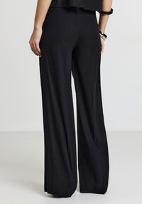 Pantalons noirs à jambes larges en tissu doux et texturé. Conçus avec un léger brillant, présentant une coupe droite et sans poches visibles.