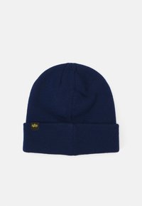 Námornícka pletená čiapka s ohnutým okrajom, s malou, prišitou čiernou nášivkou s detailom žltého loga. Mäkko textúra a tesný dizajn.