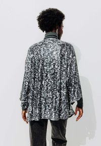 Kimono noir et blanc à motifs avec une surface texturée, coupe loose, manches larges et col montant, superposé sur un haut gris.