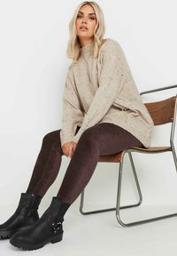 Beżowy sweter dziany z drobnymi włóknami, wysoka szyja i luźny krój. Ciemnobrązowe legginsy z korduroy. Czarne botki za kostkę z bocznym zamkiem i akcentami.