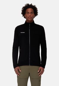 Giacca in pile nera con colletto alto, zip frontale completa e tasche con zip. Presenta un logo sul petto e un tessuto testurizzato.