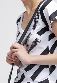 Černobílá krátká košile s abstraktními vzory a puntíky. Materiál vypadá jemně a lehce, s kulatým výstřihem.