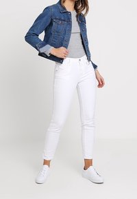 Džínová bunda v modré barvě, světle šedé tričko a bílé úzké džíny. Bílé tenisky. Klasický outfit s obepnutým siluetou.