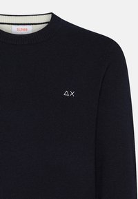 Maglione lavorato a maglia blu navy con scollo rotondo. Presenta un piccolo logo ricamato bianco sul petto e un colletto a coste. Il materiale sembra morbido.