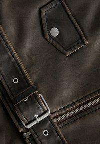 Close-up of dark brown leather jacket showing metal snap button, zipper, and belt with silver buckle and grommets.
