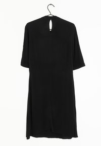 Černé šaty s krátkými rukávy, měkká látka, rovný střih a detail v podobě klíčové dírky na zadní straně. Visí na černém háčku na bílém pozadí.