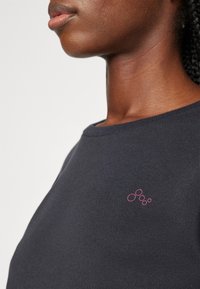 Mørk marineblå hettegenser med rund hals, med en liten rosa sirkulær logo på venstre bryst. Glatt tekstur.