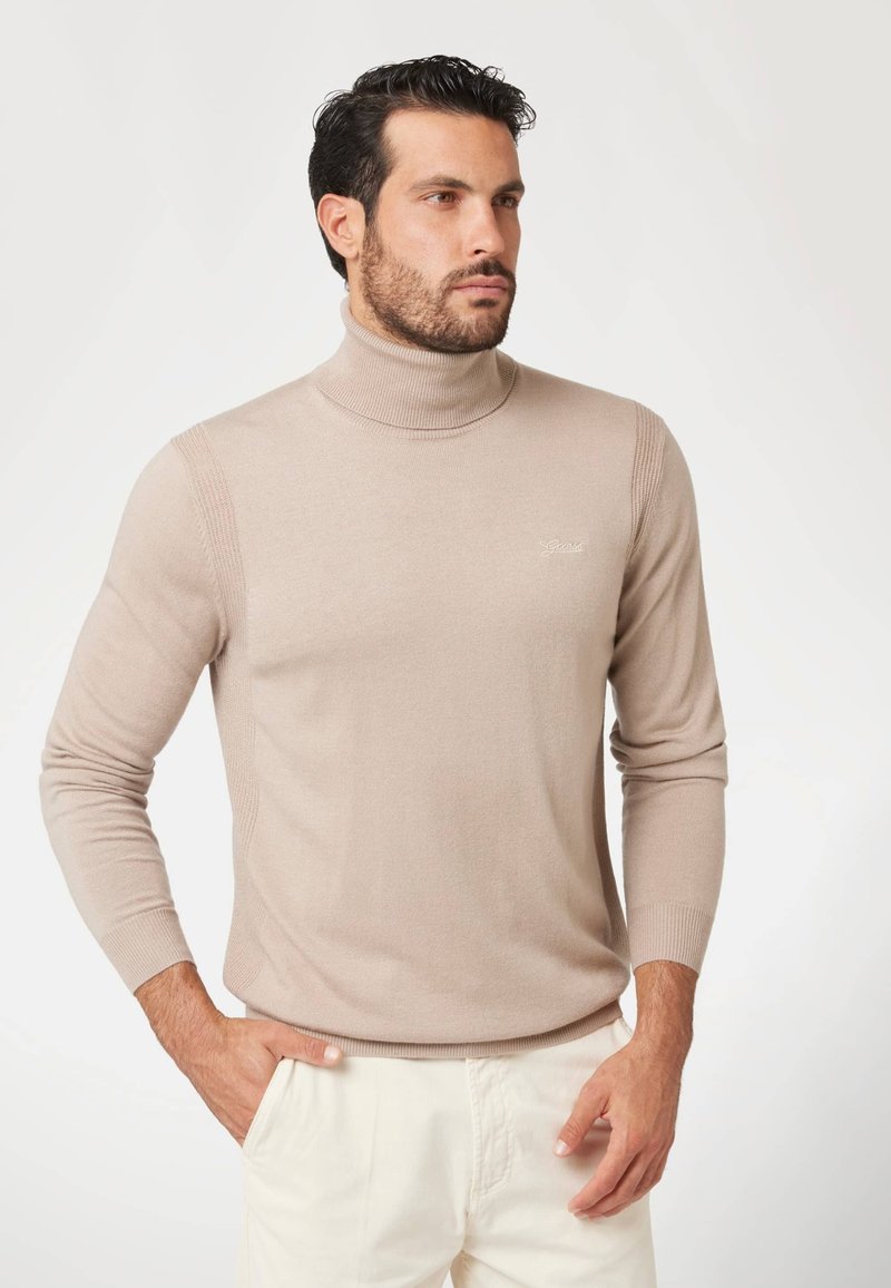 Maglione a collo alto beige in un morbido tessuto a maglia. Presenta dettagli a coste sul collo e sulle spalle. Maniche lunghe e aderenti.