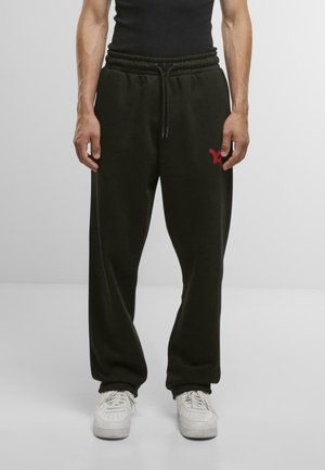 Schwarze Jogginghose mit verstellbarem Kordelzugbund, lockerer Passform und kleinem roten Logo am linken Oberschenkel. Gefertigt aus weichem Material.
