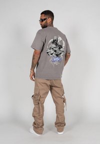 Grå oversized t-shirt med grafisk design på ryggen, parret med beige cargo-bukser, der har flere lommer og en afslappet pasform.