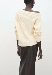 Kremfarvet strikket sweater med off-shoulder design med teksturerede diagonale kabler, kombineret med et mørkt nederdel.