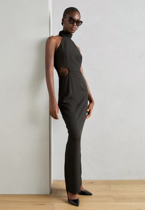 Black halter neck dress with a fitted silhouette, cut-out mesh detail at the waist, and floor-length hem. Worn with pointed black heels.