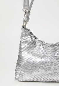 Silver sequin handbag with a curved shape, featuring a zip closure and a detachable strap. Smooth texture with metallic shine.