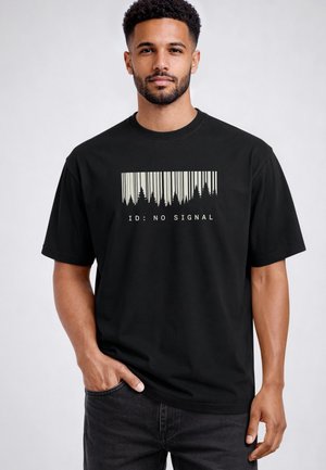 Man with short curly hair and beard wearing a black t-shirt showing a barcode design with tree silhouettes and the text "ID: NO SIGNAL."