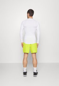 Hvid langærmet træningsskjorte og klare gule shorts. Skjorten har en tætsiddende design, og shortsene er strømlinede med lommer.
