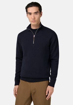 Marineblauwe zip-up trui gemaakt van zacht materiaal, met een hoge kraag, ribgebreide manchetten en zoom, in een strak, minimalistisch ontwerp.