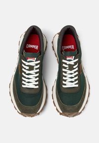 Green sneakers with white laces, featuring a textured fabric upper, brown accents, and a thick rubber sole. Red insole with "CAMPER" branding.