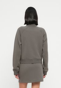 Γκρι φούτερ με στρογγυλή λαιμόκοψη, ριμπ μανσέτες και τελείωμα. Λείο ύφασμα με άνετη  εφαρμογή, φορεμένο πάνω από ένα ταιριαστό γκρι φόρεμα.