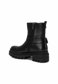 Botas negras hasta el tobillo hechas de cuero suave, con un cierre de cremallera lateral, una suela gruesa y texturizada, y una correa decorativa alrededor del tobillo.