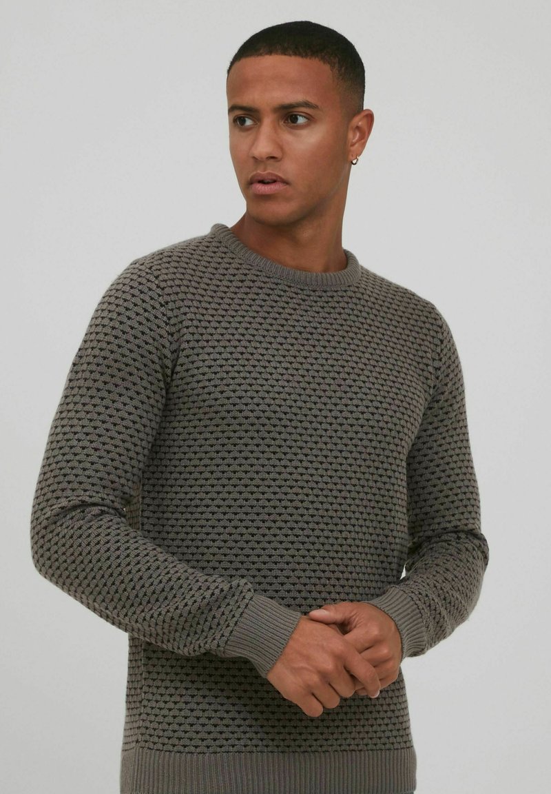 Pull en maille gris texturé avec un col rond et des poignets côtelés. Le motif présente de petites motifs en relief sur le tissu.