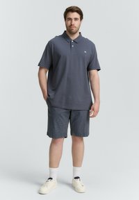 Graues Polohemd mit Kragen, kombiniert mit dunkelblauen Jeansshorts. Weiße Sneakers und Socken vervollständigen das Outfit. Einfaches, lässiges Design.