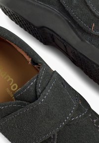 Scarpa slip-on in suede nero con suola strutturata, caratterizzata da accenti cuciti e una fascia in velcro per una vestibilità sicura. Fodera interna in pelle marrone.