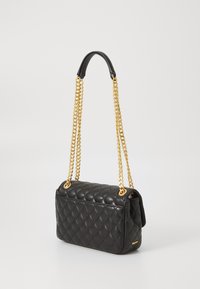 Black quilted handbag with gold chain straps. Rectangular shape, smooth texture, featuring a flap closure and logo accent on one side.