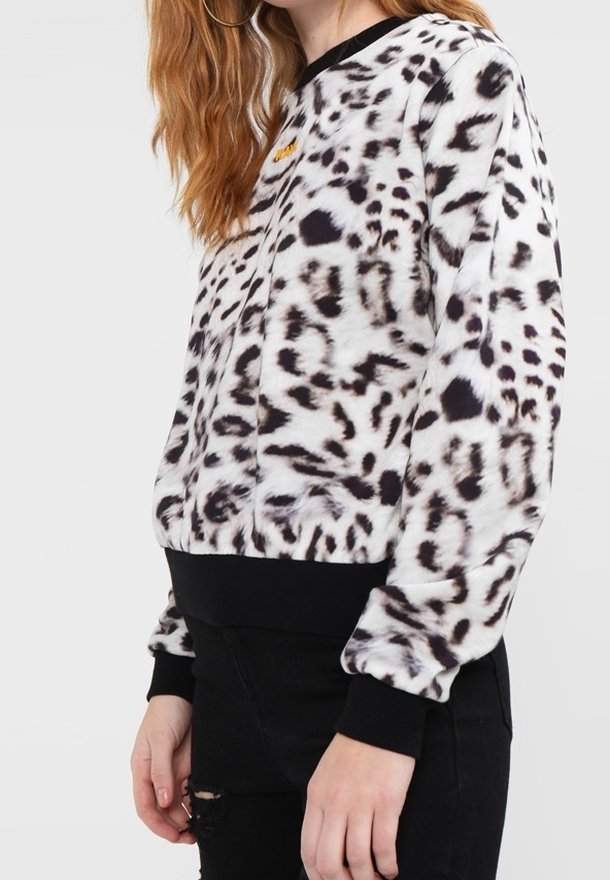 Mujer vistiendo un sudadera de leopardo blanco y negro con puños y dobladillo negros, combinada con unos jeans negros desgastados.