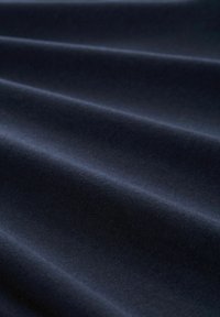 Tissu bleu foncé avec une texture douce et lisse, présenté en plis doux créant des lignes diagonales et des ombres subtiles.