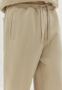 Beige sweatpants van zacht materiaal, met een elastische tailleband met een trekkoord en twee zijzakken met platte randen.