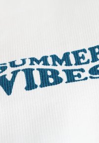 Witte stof met blauwe geborduurde tekst "SUMMER VIBES." De textuur is glad met een subtiel geribbeld patroon.