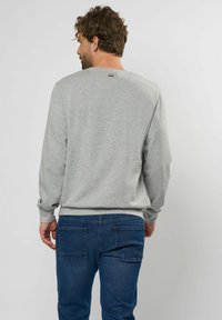 Grijze sweatshirt met lange mouwen, geribbelde manchetten en tailleband. Heeft een klein embleem op de achterkant van de halslijn, gecombineerd met blauwe jeans.
