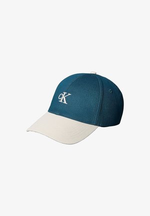 Gorra hecha de tela azul y crema, presenta una corona redondeada, una visera curvada y un logo "cK" bordado en blanco en la parte frontal.