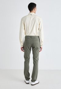 Light yellow button-up shirt with long sleeves, paired with olive green tailored pants and white sneakers, shown from the back.