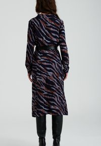Robe à manches longues en tissu marine foncé avec un motif de rayures de tigre marron et bleu clair, cintrée à la taille avec une ceinture noire.