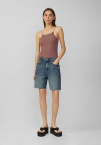 Brązowy bezrękawnik na cienkich ramiączkach, w połączeniu z niebieskimi dżinsowymi szortami z postrzępionymi brzegami oraz czarnymi sandałami na platformie.